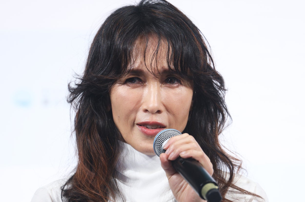 女性が白いトップスを着てマイクを持ち話している。