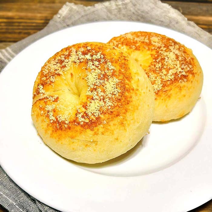 白い皿の上に、チーズがかかった2つの焼きたてのベーグルが置かれている。