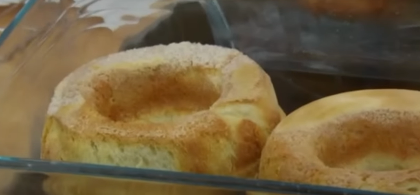 Two Yorkshire puddings in a glass baking dish, each with a sunken center and a fluffy, uneven edge