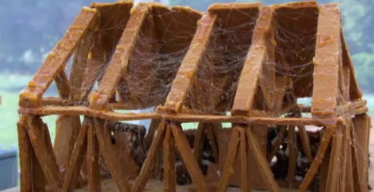 Gingerbread structure resembling a barn, decorated with cobwebs for a Halloween-themed event