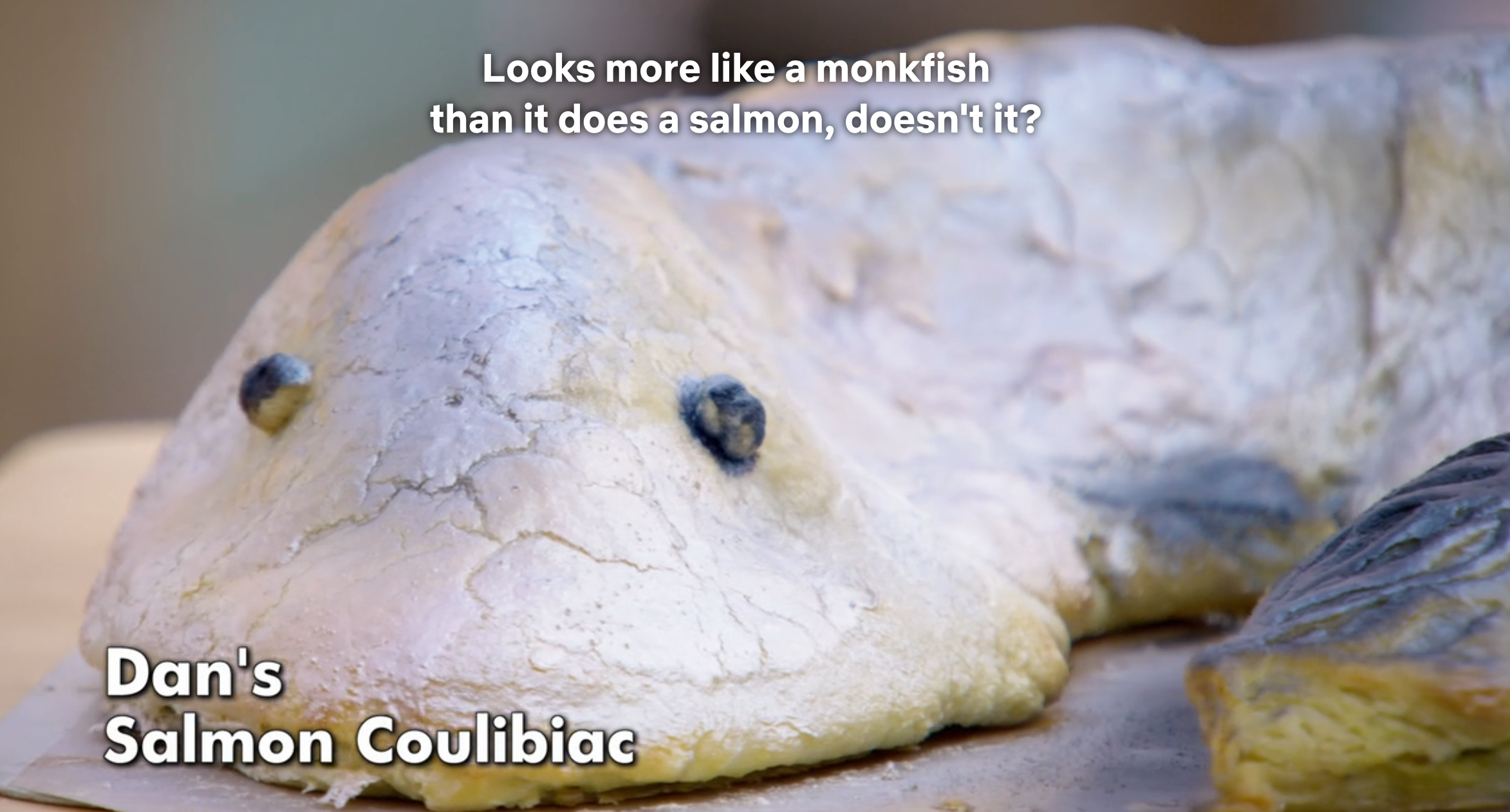 A baked salmon coulibiac is shaped like a fish, appearing more like a monkfish than a salmon. Text comments on its resemblance