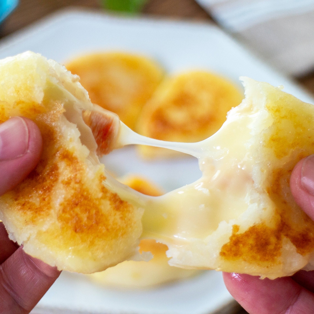 誰かがチーズ入りの焼きパンを半分に割っている様子。とろけるチーズが見える。