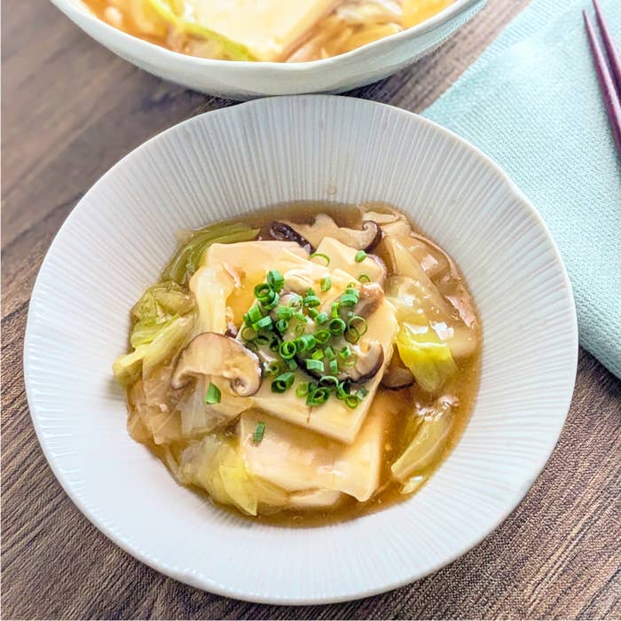豆腐とキャベツの中華あんかけ。豆腐としいたけ、キャベツとネギがトッピングされた料理のクローズアップイメージ。食卓に置かれている。