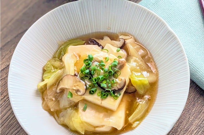 豆腐ときのこのあんかけ料理が白い皿に盛られています。ネギがトッピングされています。