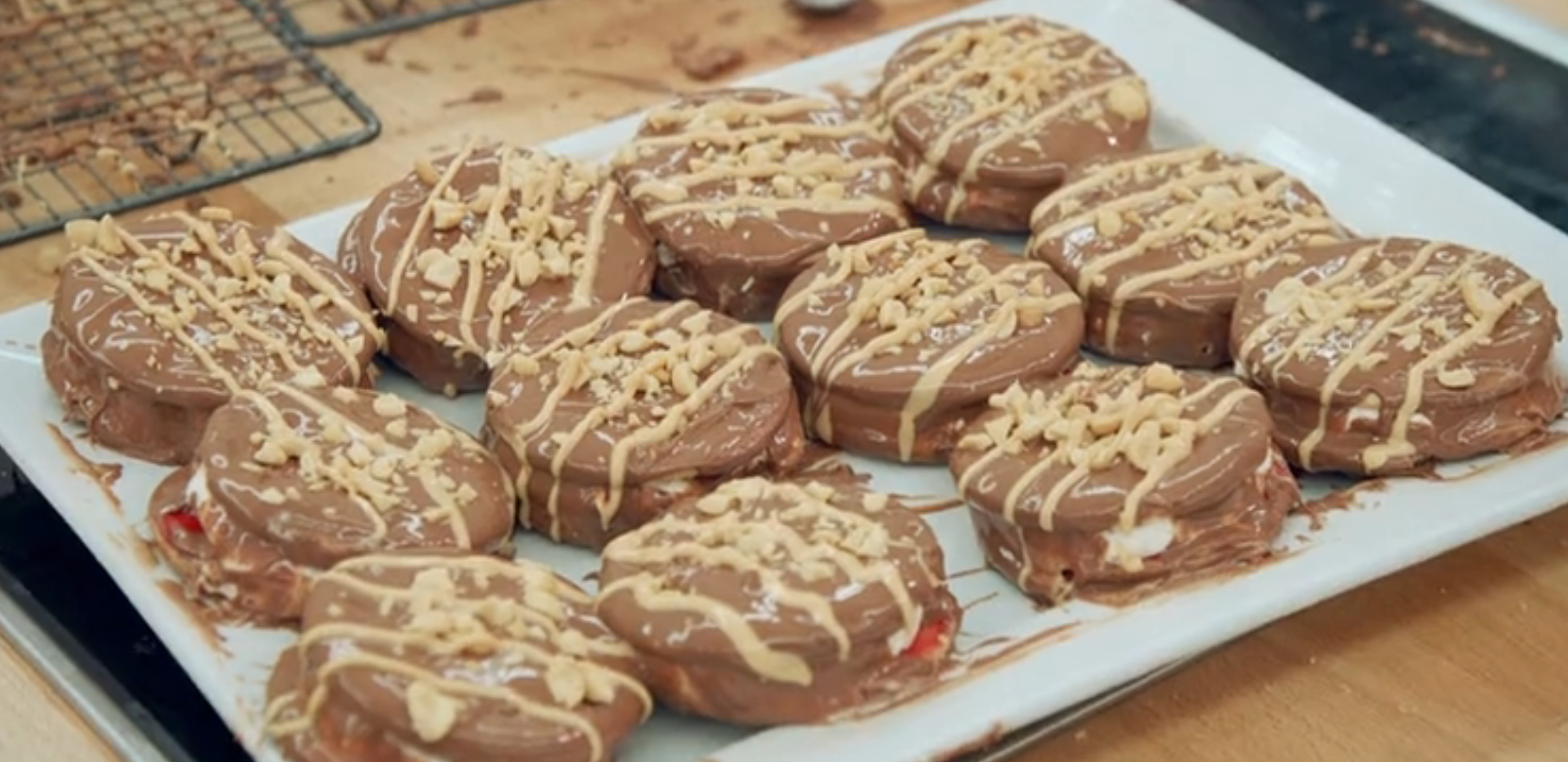 A plate of chocolate-covered cookies with drizzles and nut toppings arranged in rows