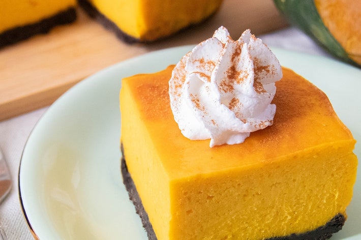 ホイップクリームをのせたかぼちゃのチーズケーキが皿に盛られています。背景に切ったかぼちゃと残りのチーズケーキが見えます。