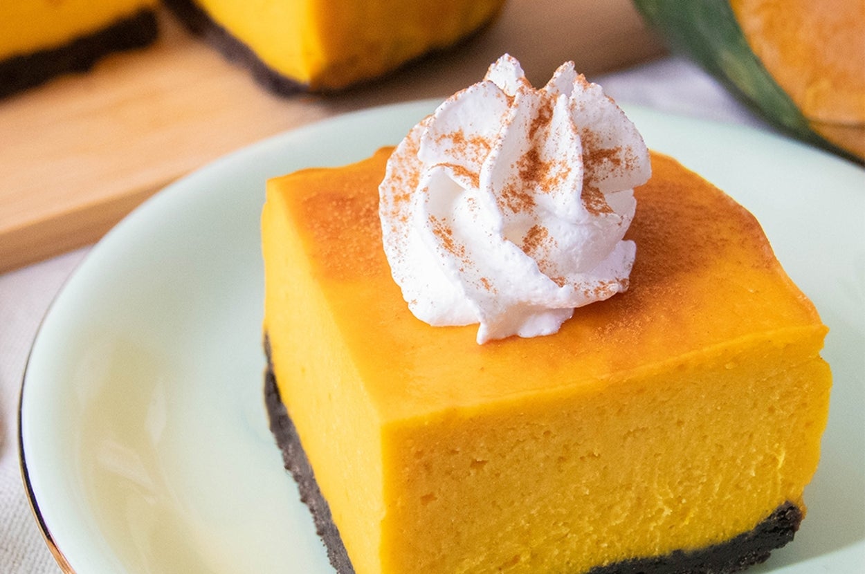 ホイップクリームをのせたかぼちゃのチーズケーキが皿に盛られています。背景に切ったかぼちゃと残りのチーズケーキが見えます。