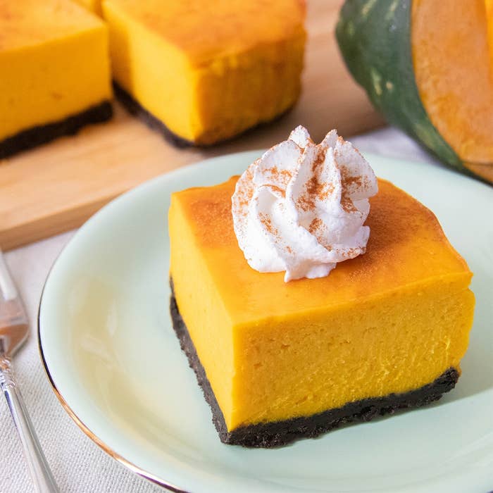 ホイップクリームをのせたかぼちゃのチーズケーキが皿に盛られています。背景に切ったかぼちゃと残りのチーズケーキが見えます。
