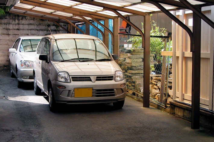 2台の車がカーポートに駐車されている。背景にフェンスと植栽が見える。