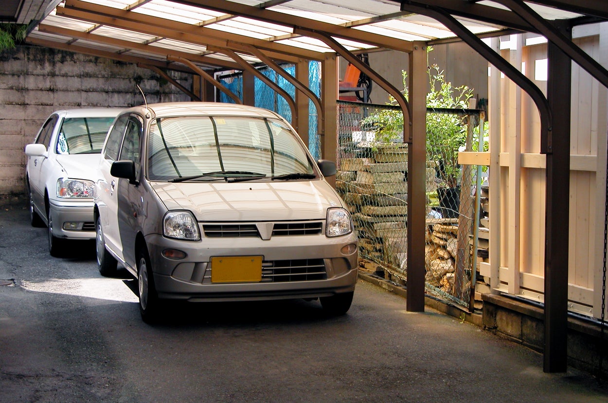 2台の車がカーポートに駐車されている。背景にフェンスと植栽が見える。