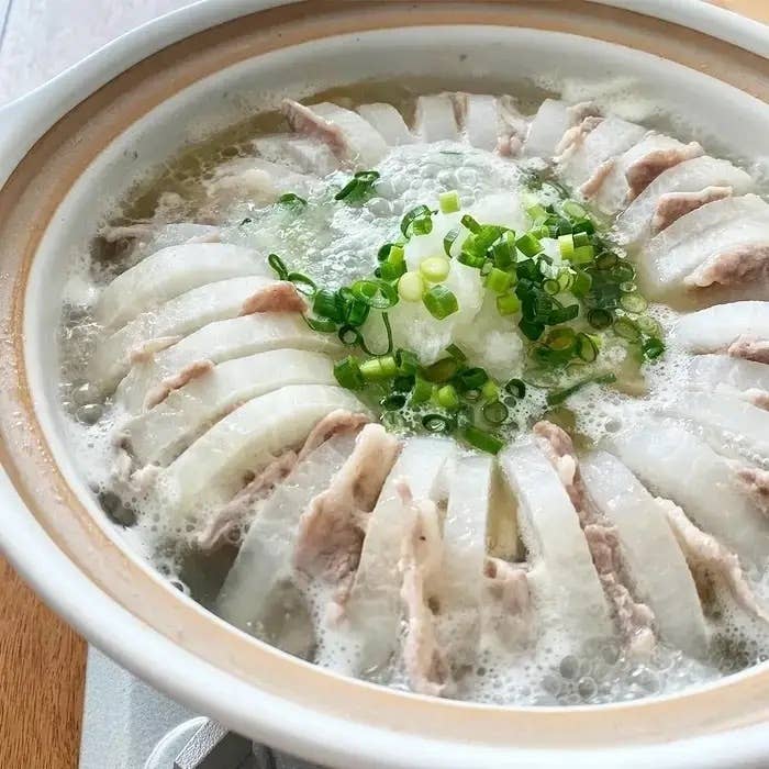 鍋に整然と並べられた薄切りの大根と豚肉が煮込まれており、中央に刻みネギが載せられています。