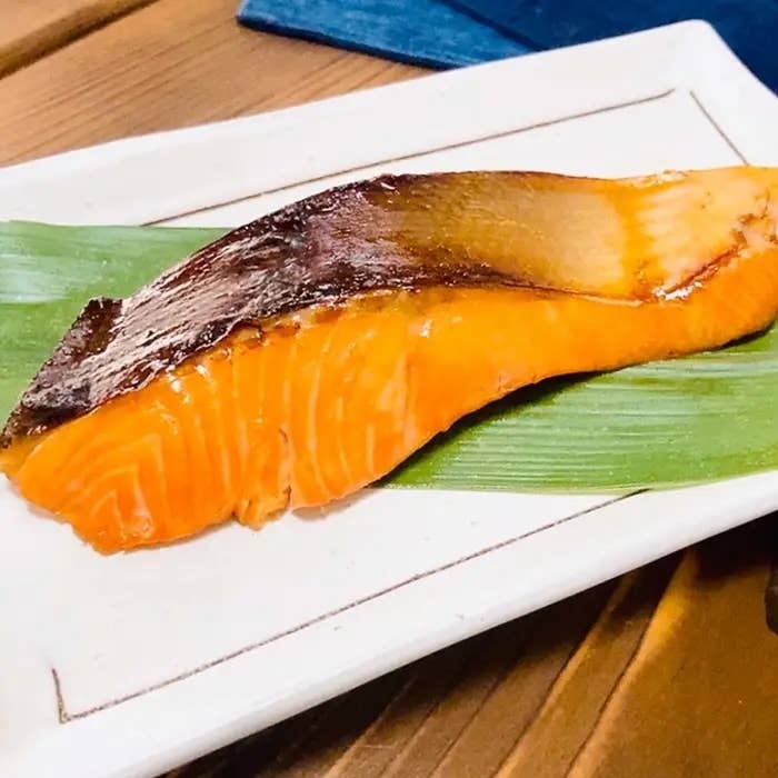 皿の上に竹の葉が敷かれ、その上に焼きサケの切り身が置かれているシンプルな料理の写真。
