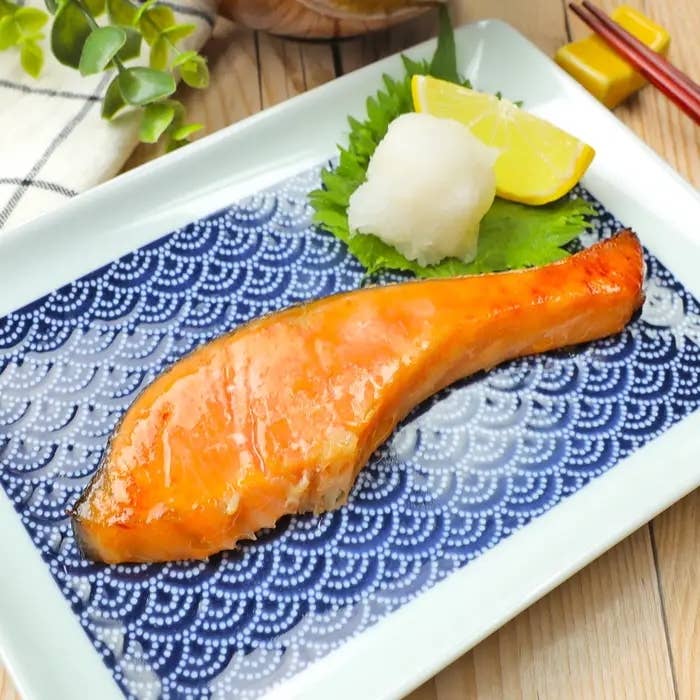 和風皿に盛られた焼きサケ、添え物に大根おろしとレモンがあり、美しくプレゼンテーションされた料理。