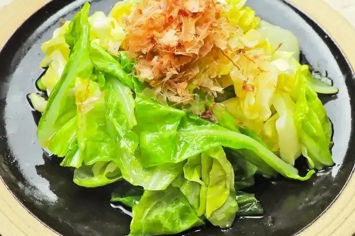 キャベツの炒め物に鰹節がトッピングされた料理が黒い皿に盛られている。