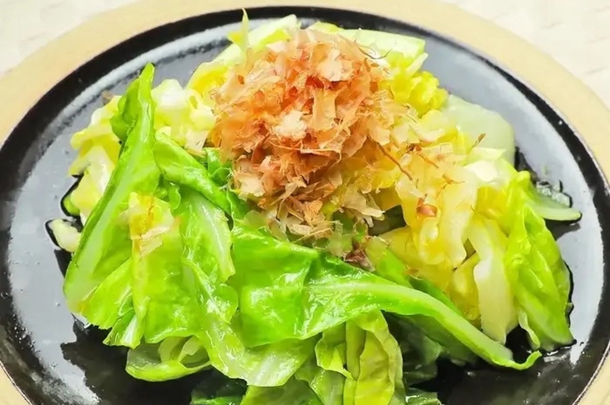 キャベツの炒め物に鰹節がトッピングされた料理が黒い皿に盛られている。
