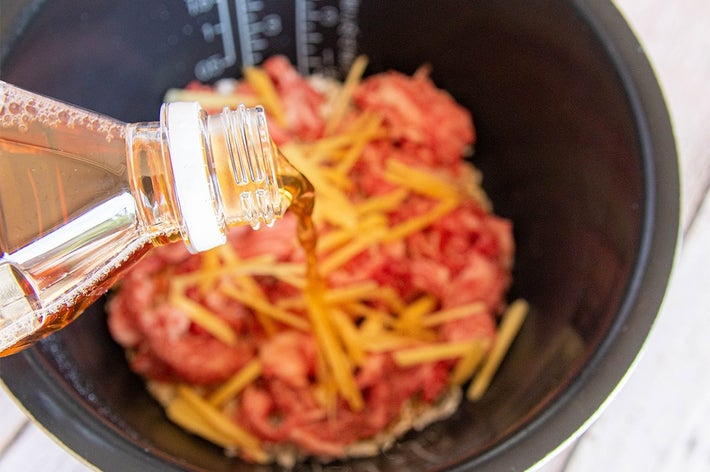 炊飯器に入った肉と生姜と米の上にほうじ茶を注いでいる料理準備の様子。