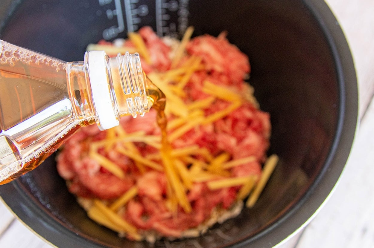 炊飯器に入った肉と生姜と米の上にほうじ茶を注いでいる料理準備の様子。
