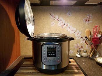 Instant Pot unit cooker with unfastened lid connected a room counter, surrounded by cooking utensils successful a modern room setting
