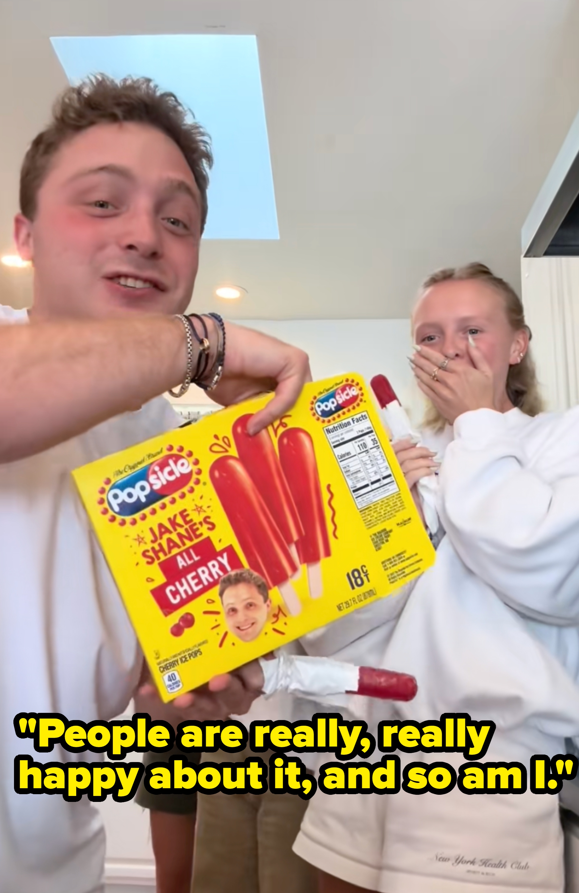 Two people smiling and holding a Popsicle box that reads "Cherry." One person holds a popsicle; the other covers their mouth in surprise or amusement