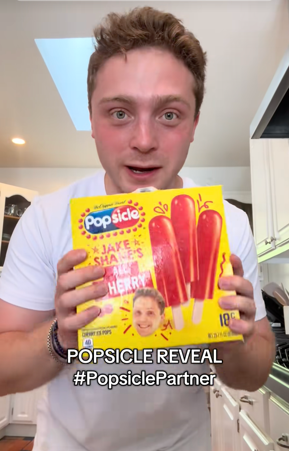 Jake holds a box of Popsicles featuring Jake Shane promoting a cherry flavor in a kitchen. Text: "POPSICLE REVEAL #PopsiclePartner."