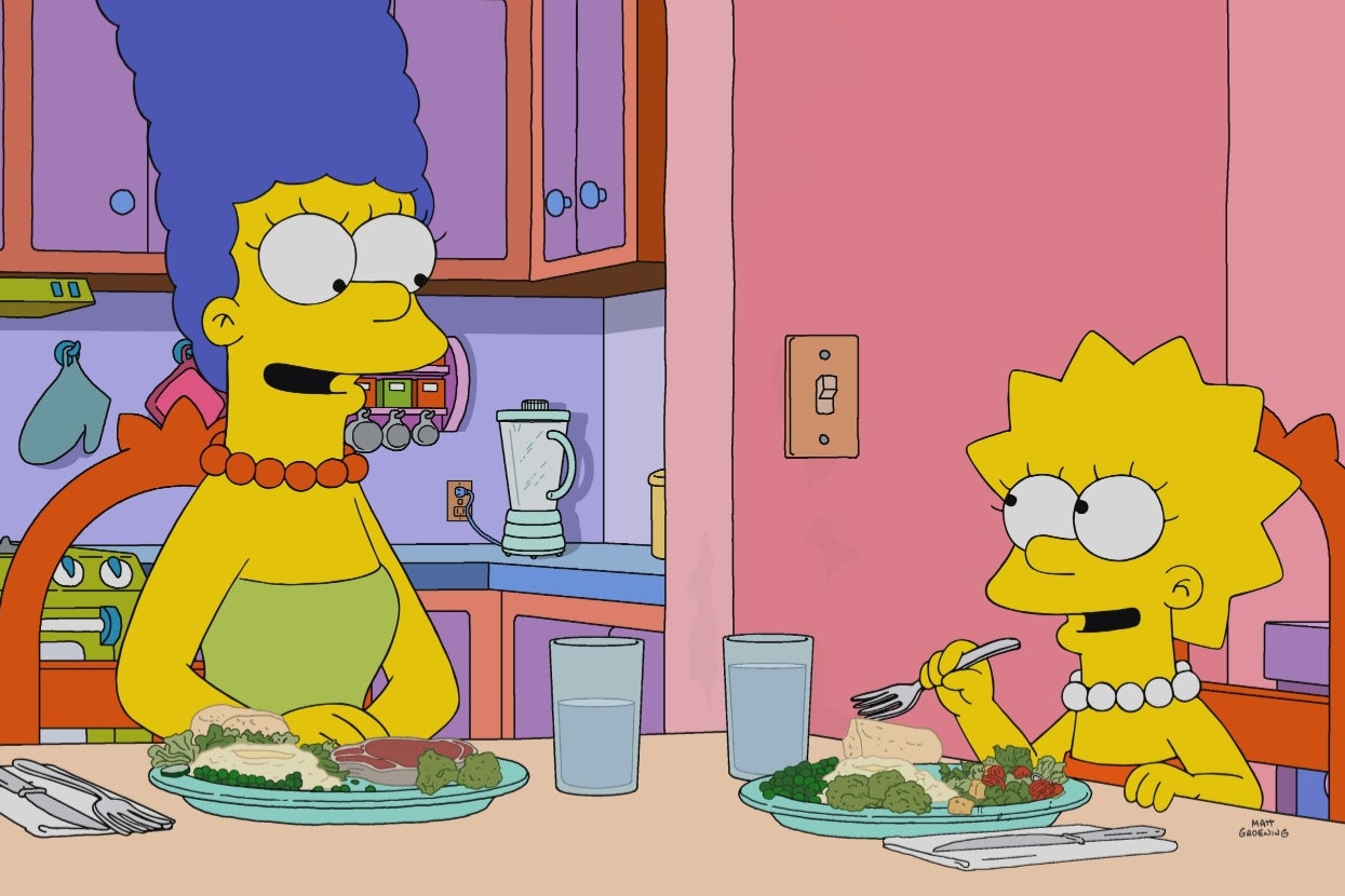 Marge and Lisa Simpson are sitting at a kitchen table, sharing a meal and smiling at each other