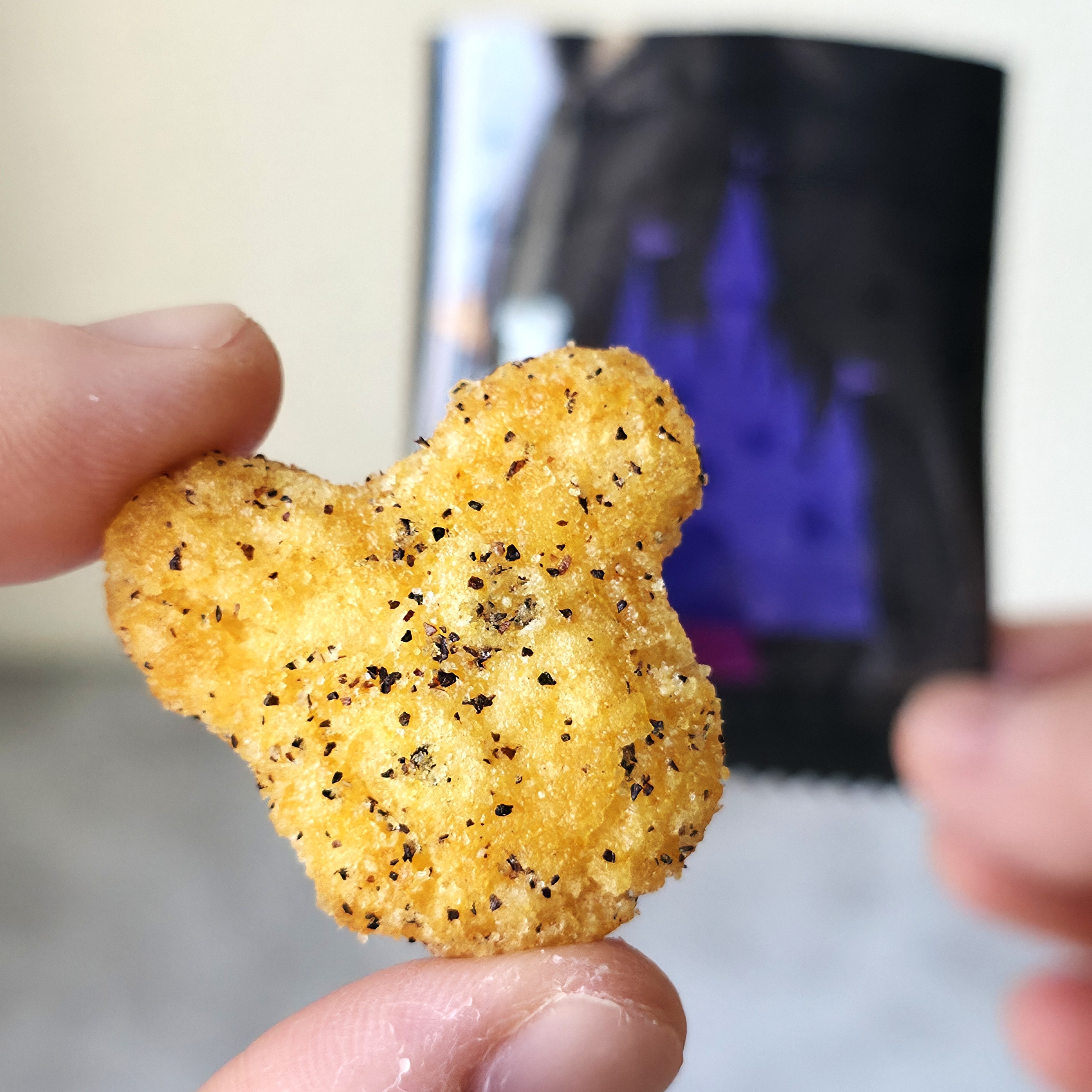 ネズミの形をしたスナックが指でつままれている。背景には紫色の城のイラストが描かれたパッケージ。