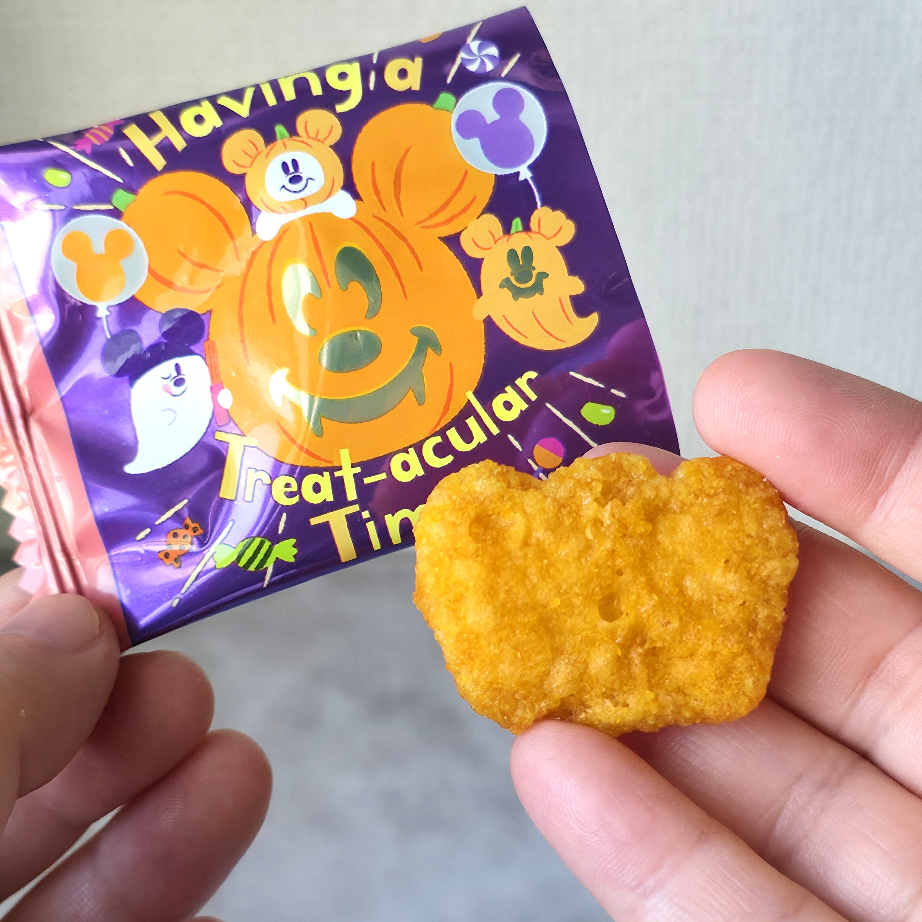 ハロウィンの詰め合わせ袋を持つ手。袋にはかぼちゃのイメージがあり、ミッキー型のスナックが手に載せられている。