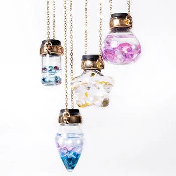 Necklaces with small, wide bottles filled with colorful crystals, hanging from golden chains. Suitable for adding a whimsical interaction to outfits