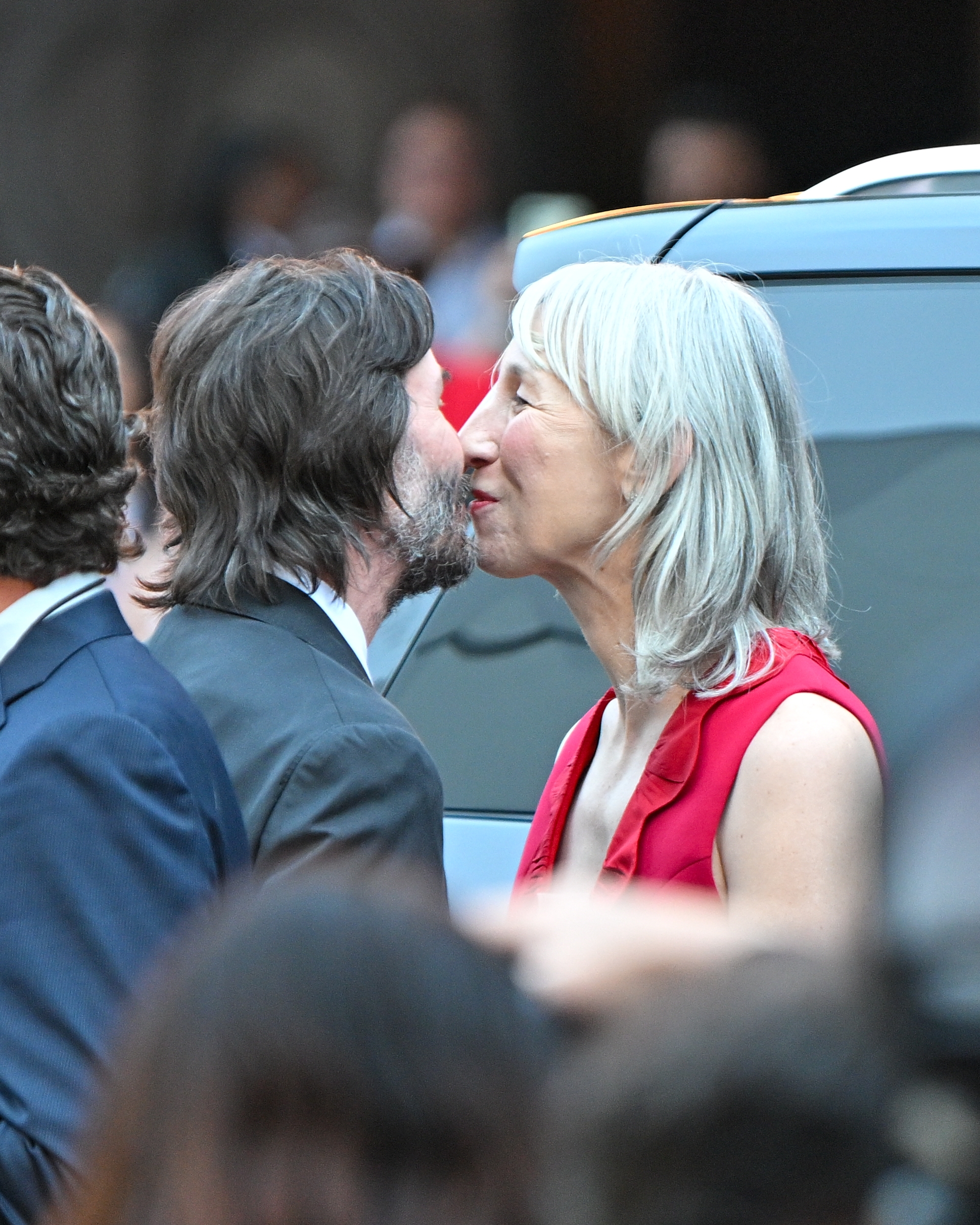 Keanu Reeves and Alexandra Grant lean in for a kiss while standing near a vehicle