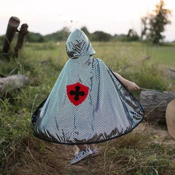 Child wearing a shiny, dotted superhero cape with a awesome connected the back, walking successful a grassy field