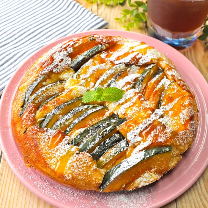 かぼちゃのスイーツタルトがピンクの皿に載っており、上に粉砂糖とミントの葉が飾られています。