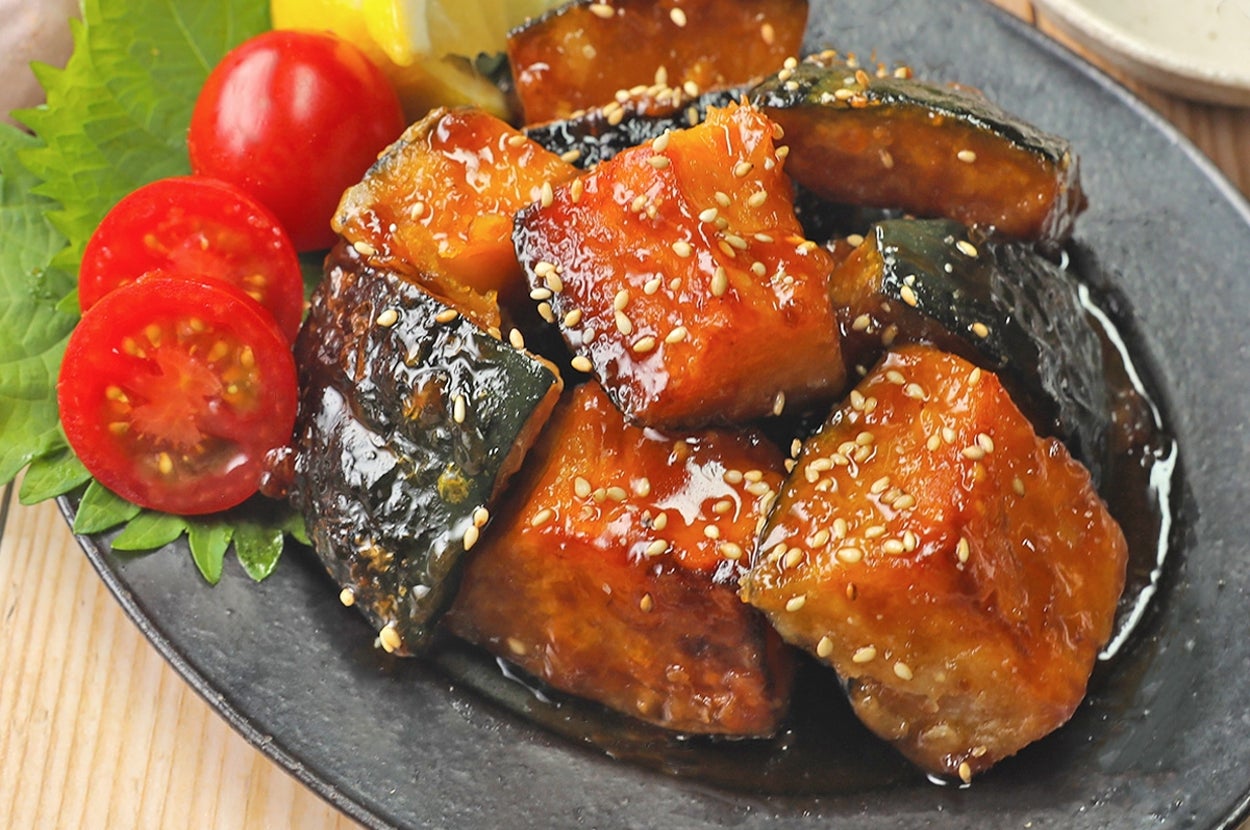 黒い皿に盛られた照り焼きソースがかかったカボチャと豆腐。添えられたプチトマトとレモンが彩りを添えている。