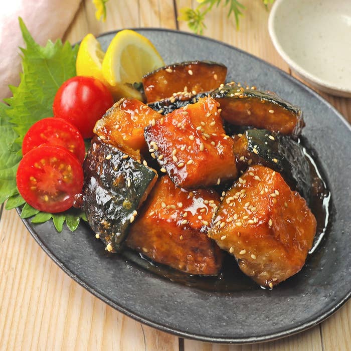 黒い皿に盛られた照り焼きソースがかかったカボチャと豆腐。添えられたプチトマトとレモンが彩りを添えている。