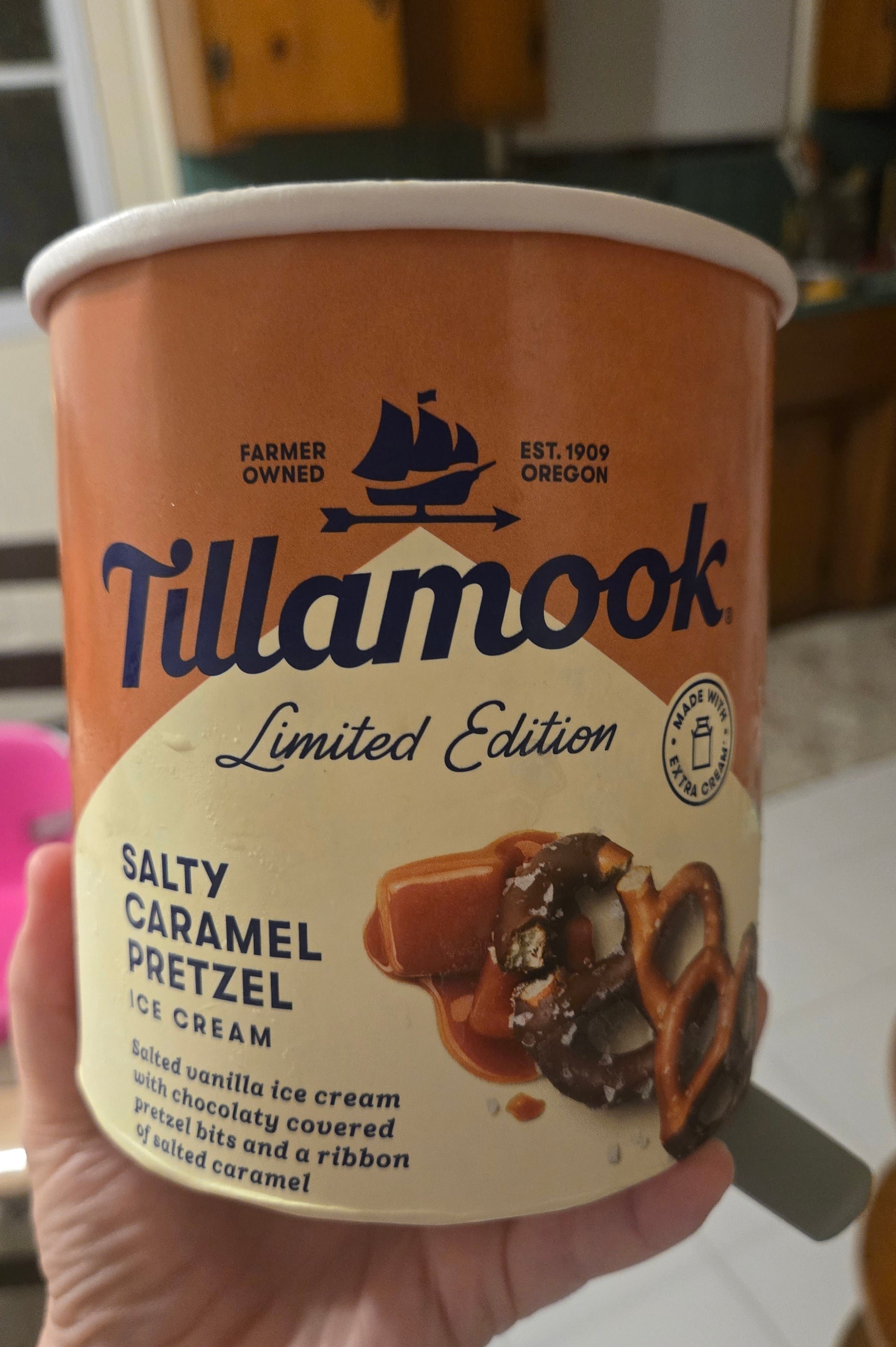 A hand holds a container of Tillamook Limited Edition Salty Caramel Pretzel ice cream