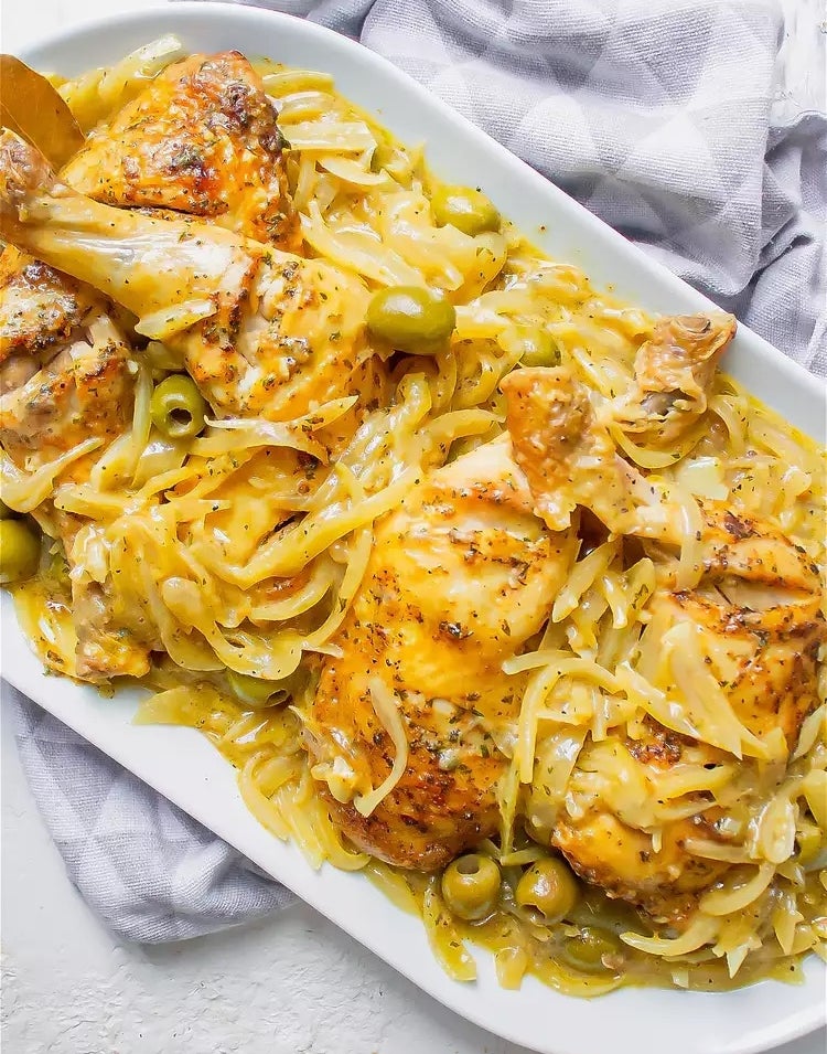 Chicken thighs baked with onions and green olives, garnished with herbs, served on a white platter