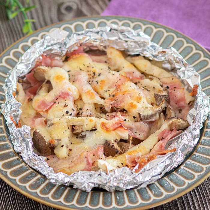 アルミホイルに包まれたベーコンとキノコのチーズ焼き料理。