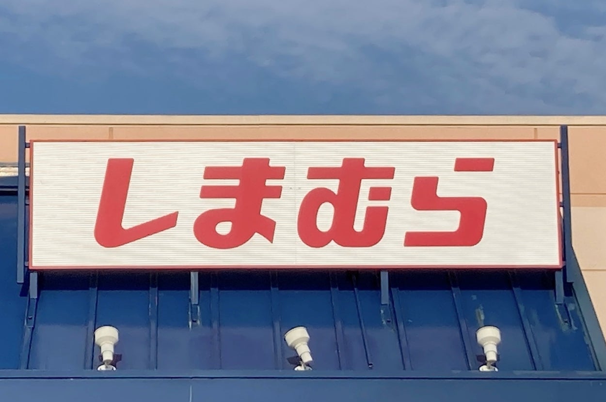 Storefront with large Japanese text reading "しまむら" above the entrance, against a blue sky background