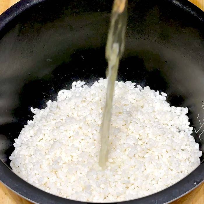 炊飯器の中に白米が入り、その上に液体が注がれている様子。