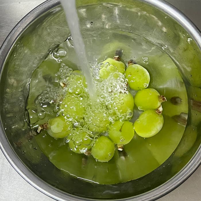 ボウルで水に浸された半分に切った緑の果物。流水が果物を洗っています。