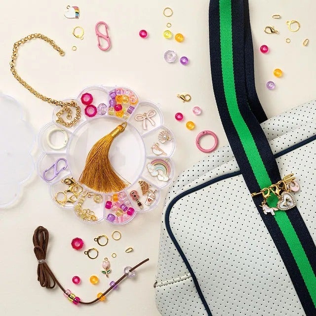 Assorted jewelry-making supplies are displayed adjacent  to a achromatic  container  with greenish  and navy straps, featuring charm accessories