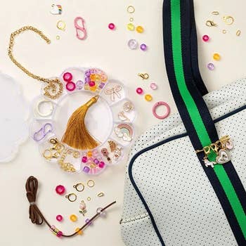Assorted jewelry-making supplies are displayed adjacent to a achromatic container with greenish and navy straps, featuring charm accessories