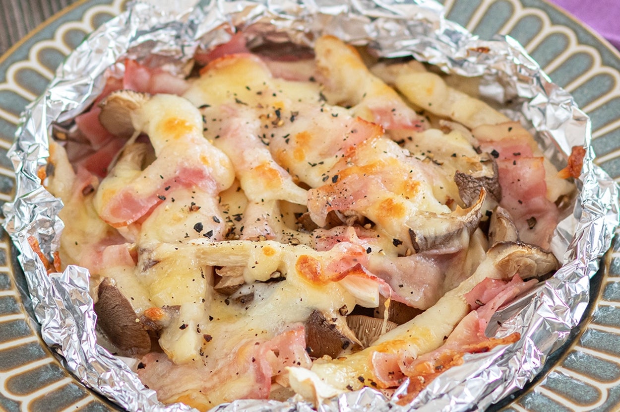 ベーコンとキノコがチーズで焼かれ、アルミホイルに包まれた料理が皿に盛られている。