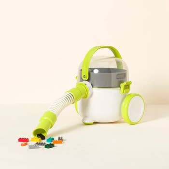 Toy vacuum cleaner with a hose, designed to prime up tiny gathering blocks, shown adjacent to colorful artifact pieces