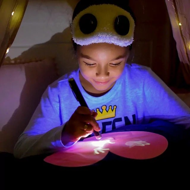 Child utilizing a glowing pen to gully  connected  a magic drafting  pillow successful  a cozy tent. Wearing a fuzzy slumber  disguise  with carnivore  ears. Ideal for originative  play