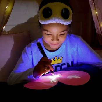 Child utilizing a glowing pen to gully connected a magic drafting pillow successful a cozy tent. Wearing a fuzzy slumber disguise with carnivore ears. Ideal for originative play