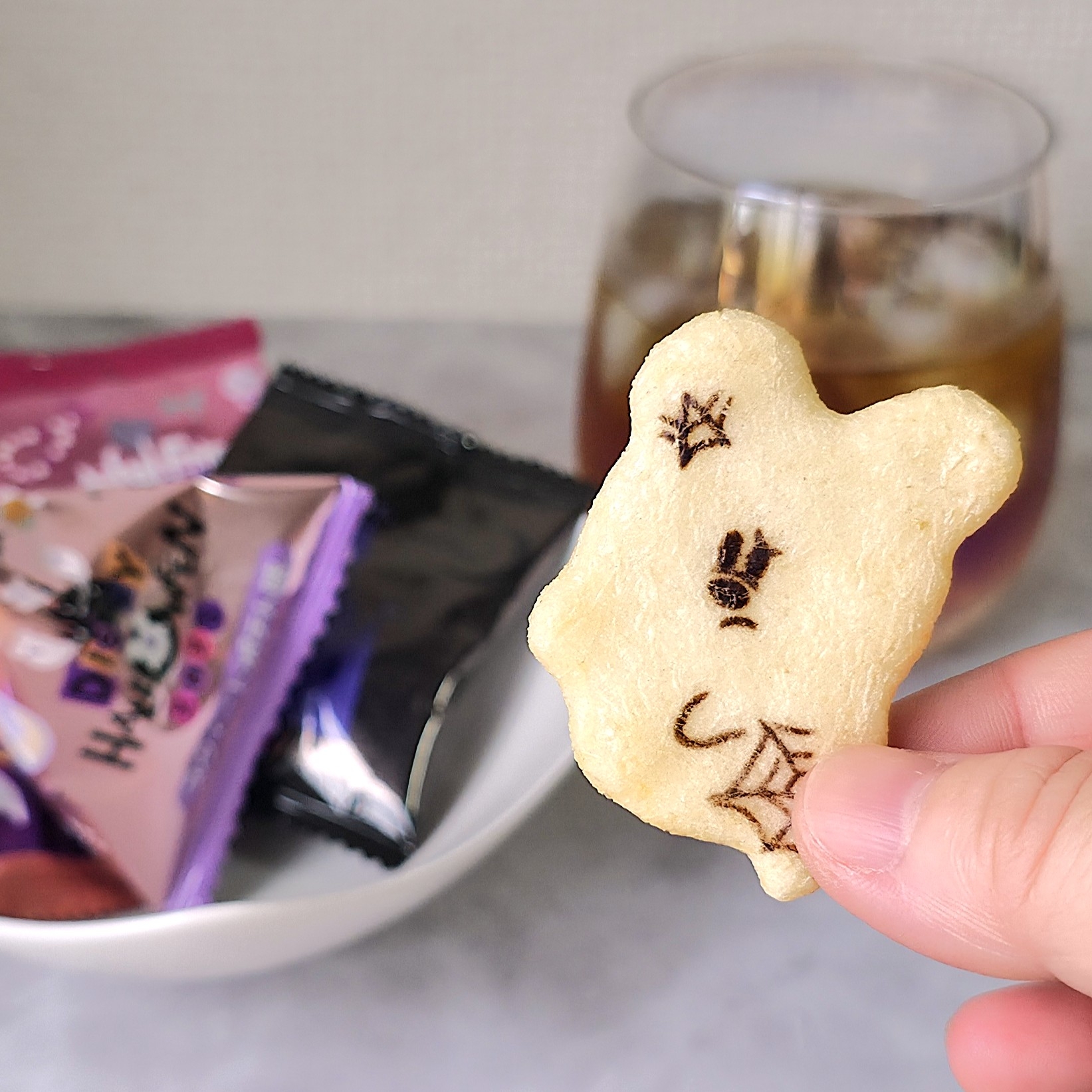 コアラの形をしたスナックを指で持ち、後ろにスナックの袋とドリンクがある。