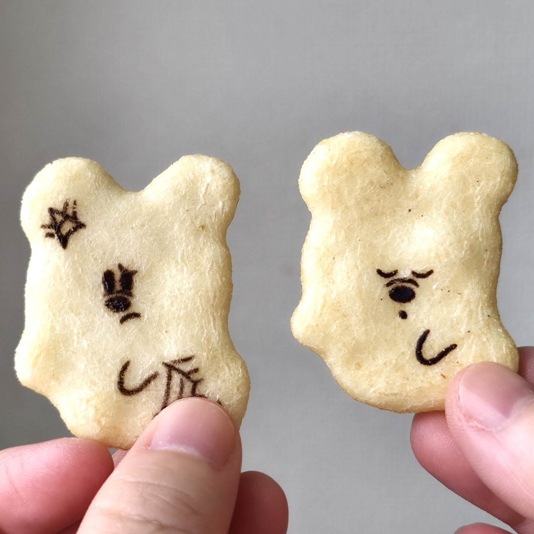2つのクマ型クッキーを手で持っている。1つは怒った顔、もう1つは悲しそうな顔。