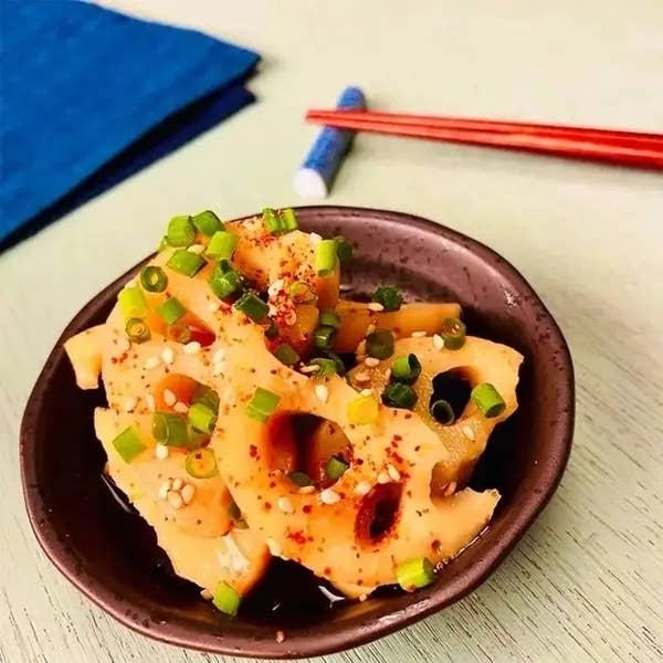レンコンの薄切りにネギを添えた和風の料理が茶色の皿に盛られています。隣に箸が置かれています。