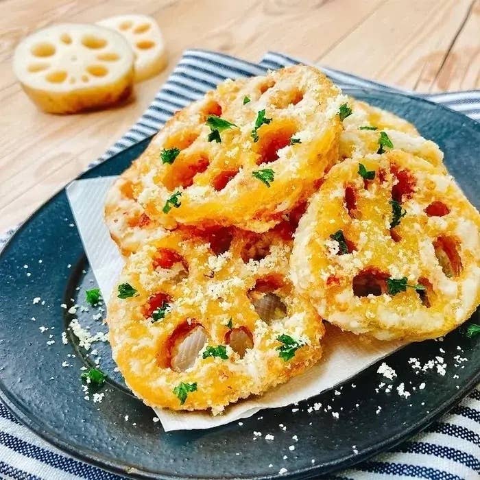 レンコンの天ぷらが黒い皿に盛り付けられ、上にパセリとパルメザンチーズがふりかけられている。