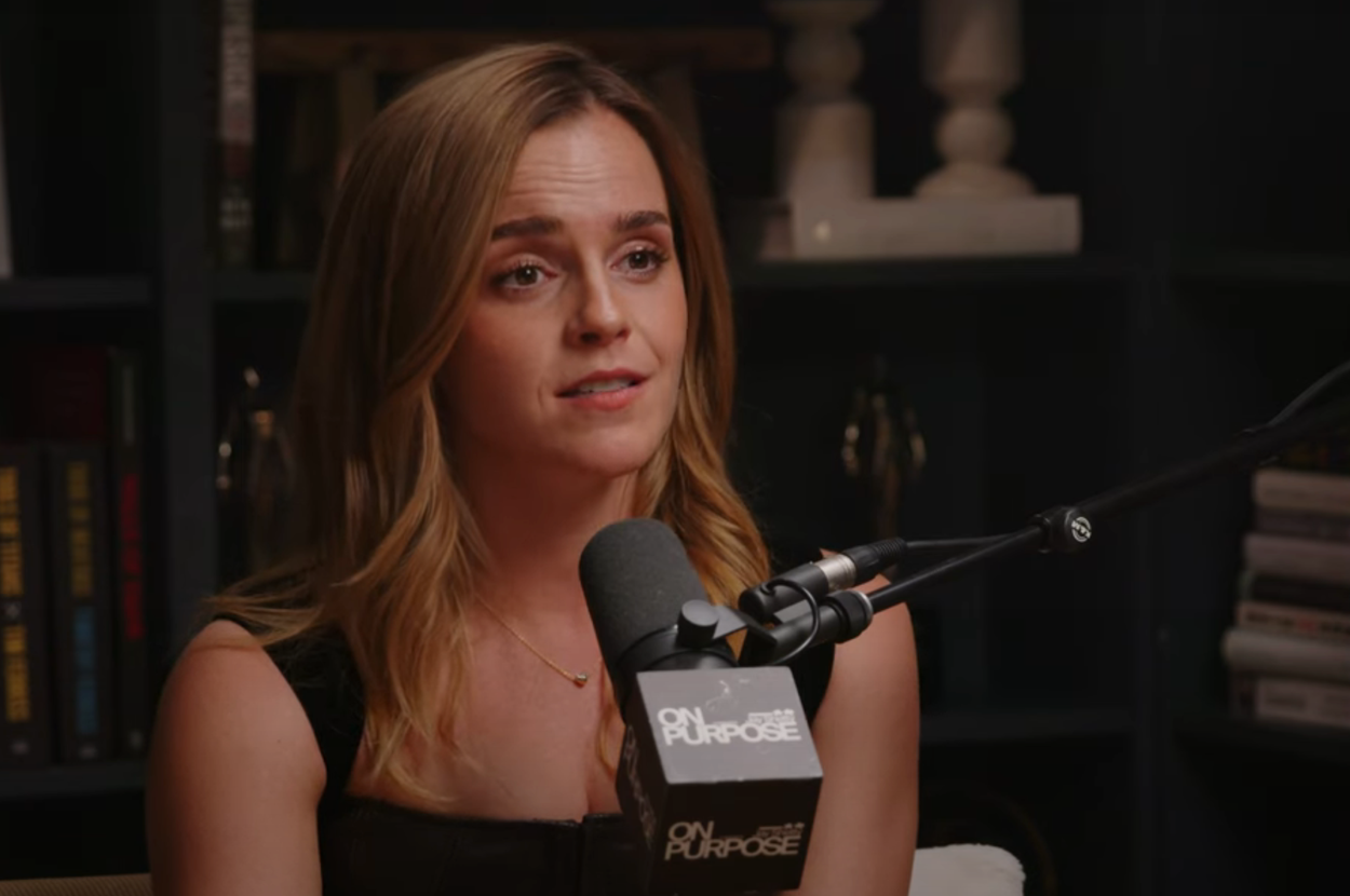 A person speaks into a microphone during a podcast interview, sitting against a backdrop of bookshelves